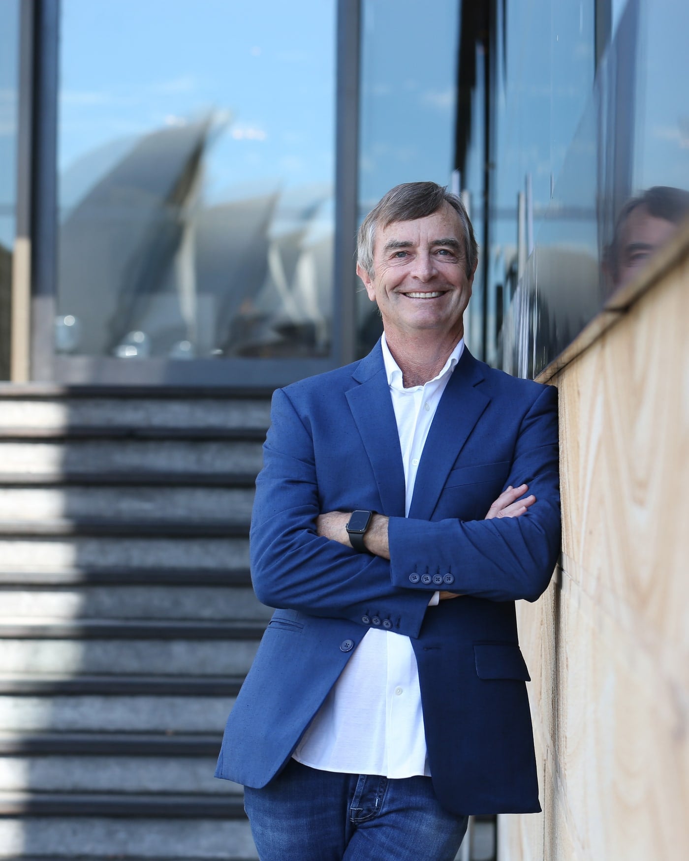 Dane Hudson, arms folded, photographed by Sydney Harbour with the Opera House behind him
